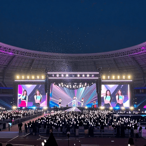 A_breathtakingly_vast_neon_stadium_stage_under_a_midnight_sky,_where_shimmering_confetti_falls_like_snow_over_a_sea_of_light-sticks